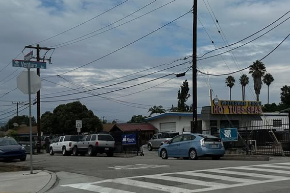 Street corner with parked cars, power lines, and cloudy sky.